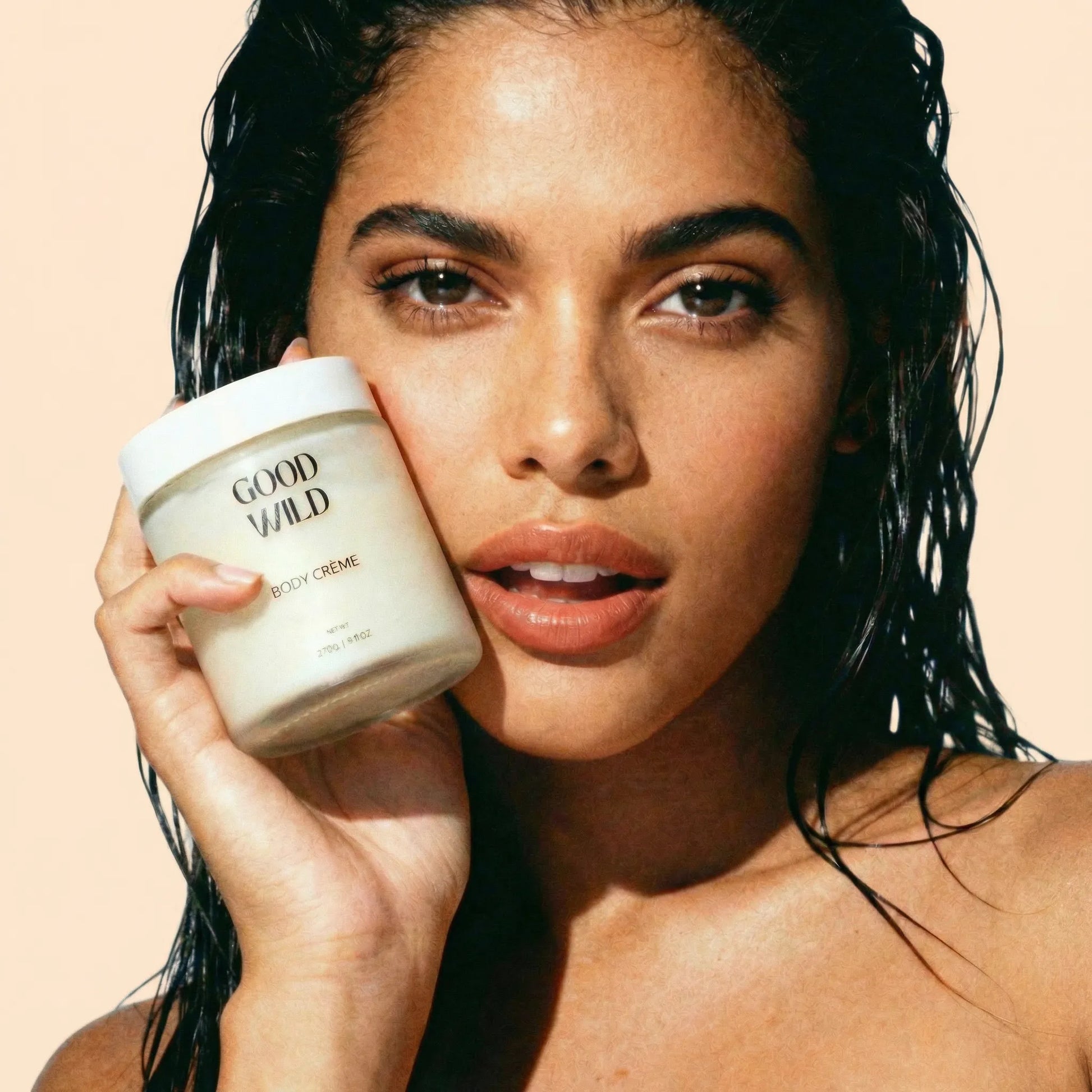 Woman holding a jar of 'Good Wild' body crème against a beige background