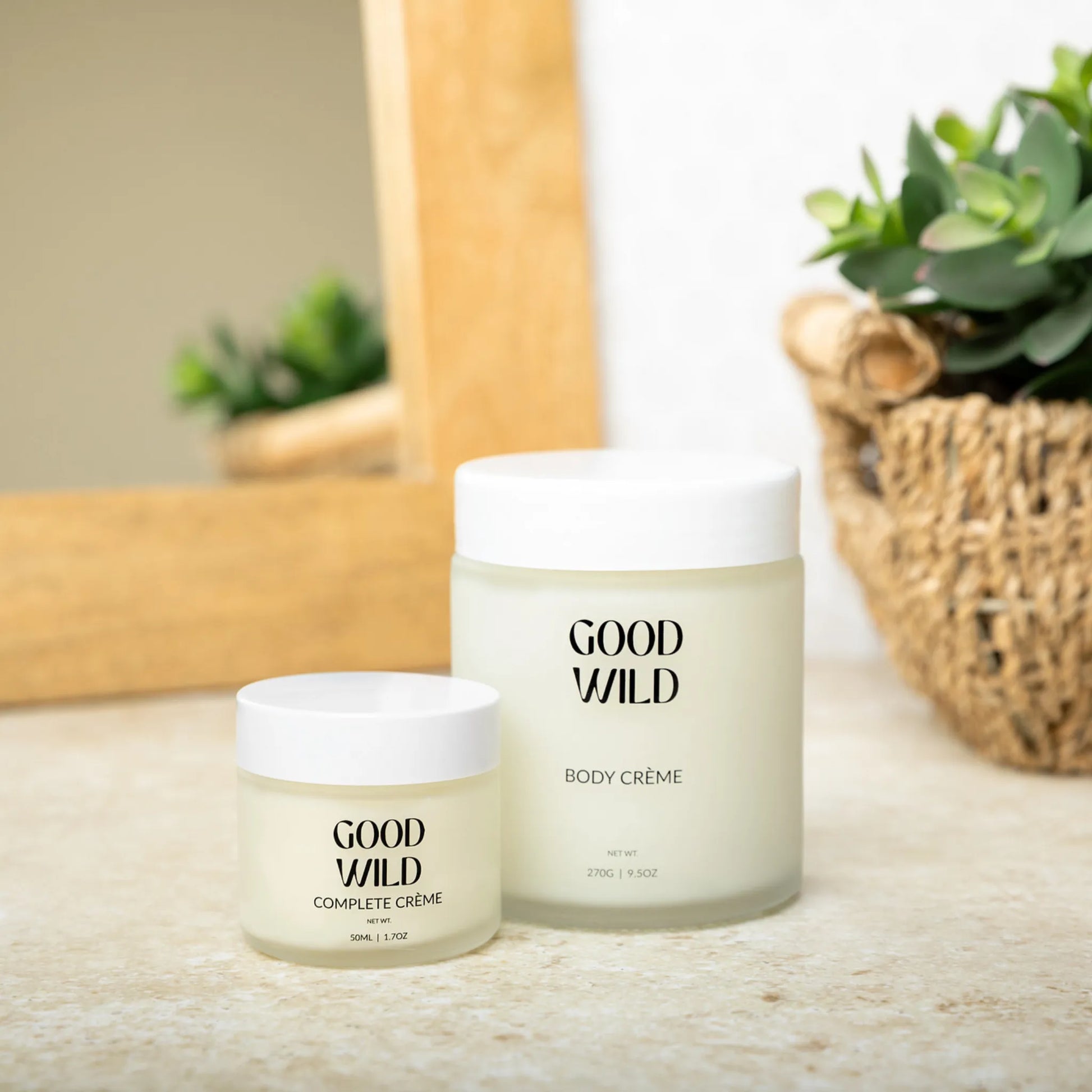 Two jars of Good Wild body crème on a surface with a plant in the background