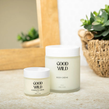 Two jars of Good Wild body crème on a surface with a plant in the background