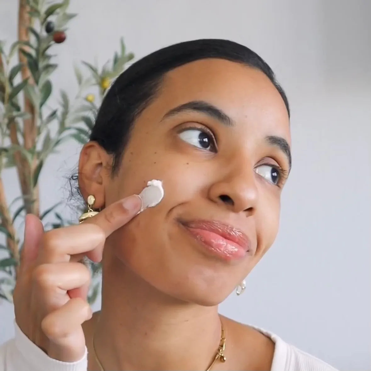 Woman applying cream to her face with a neutral background