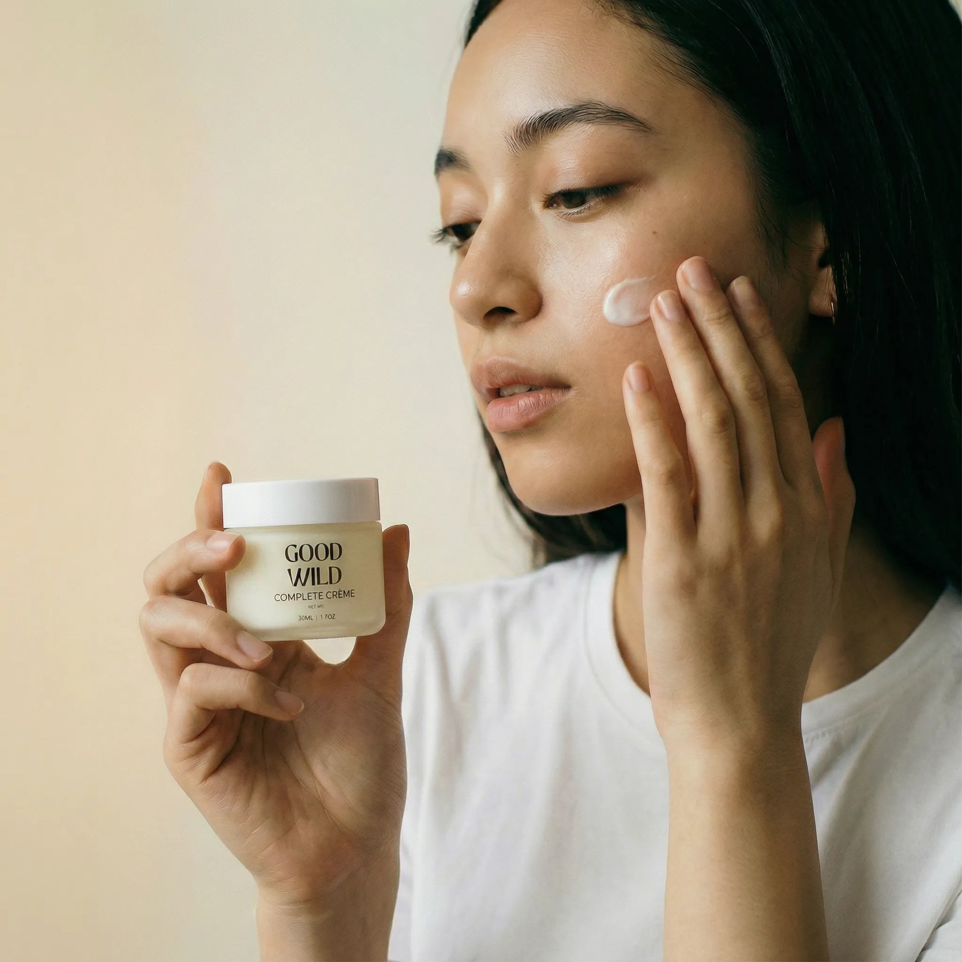 Woman applying cream to her face with a jar of 'Good on You' cream.